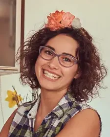 Sabrine smiling in her cozy home kitchen while preparing food, surrounded by flowers and fresh ingredients